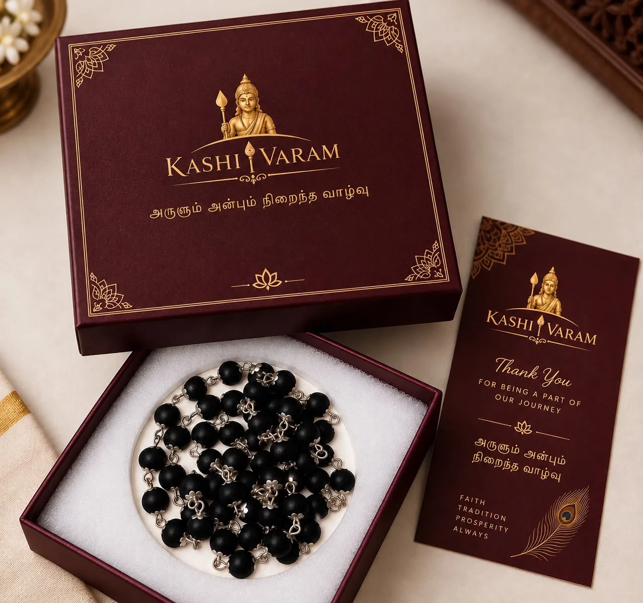 Kashi Varam maroon gift box opened to show a silver-capped karungali malai, with a thank-you card beside it